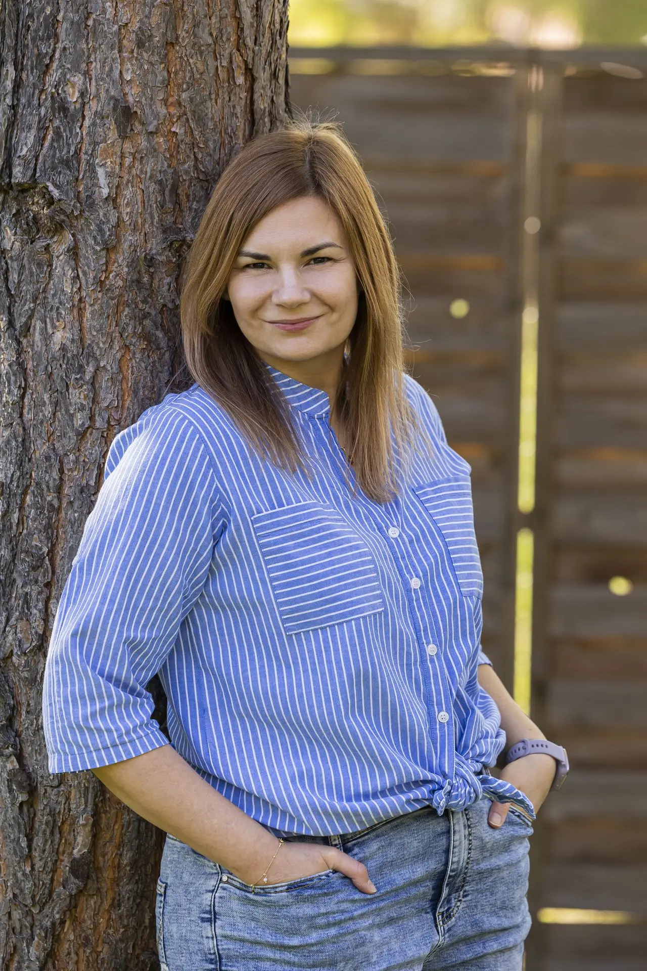 Portret uśmiechniętej Ewy opierającej się o drzewo w ogrodzie